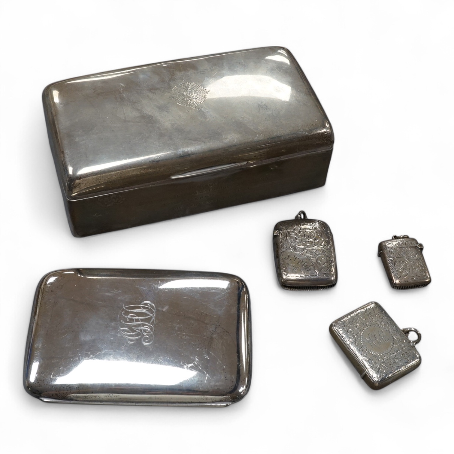 A George V silver mounted cigarette box, with engraved inscription, Deakin & Francis, Birmingham, 1926, an earlier silver cigar case and three silver vesta cases. Condition - poor to fair